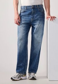 Modre jeans hlače iz jeansa z ohlapnim krojem, z zadrgo, petimi žepi in rahlo posivelimi hlačnicami. Obute so srebrni športni copati.