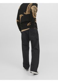 Jeans de mezclilla negra con un corte relajado, cinco bolsillos y una textura ligeramente desgastada. Combinados con un suéter estampado y zapatillas blancas.