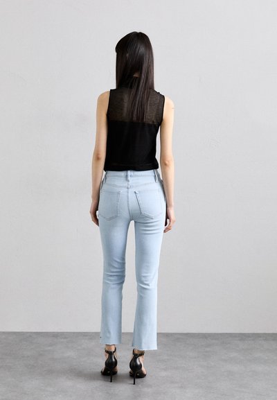 Svart uten ermer topp med gjennomsiktig rygg, paret med lyseblå skjørtjeans. Fullført med svarte hælsandaler. Glatte teksturer og avslappet passform.