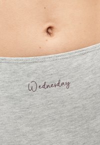 Κοντινό πλάνο γυμνού μέσης με γκρι υφασμάτινη ζώνη μέσης με την επιγραφή «Wednesday» ακριβώς κάτω από τον ομφαλό.