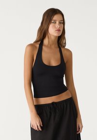 Black halter top made of smooth fabric, featuring a scoop neckline and fitted shape, paired with a flowing black skirt.