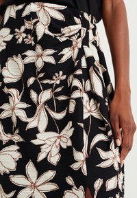 Květinová zavinovací sukně v černé barvě, se smetanovými a hnědými květinovými vzory. Texturovaná látka s drapérií a bočními rozparky.