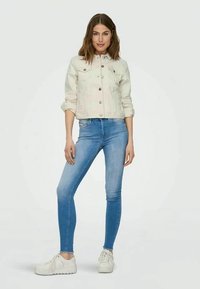Hellgraue, kurz geschnittene Jeansjacke mit Vorderknöpfen und zwei Brusttaschen. Kombiniert mit eng anliegenden blauen Jeans und weißen Sneakers.