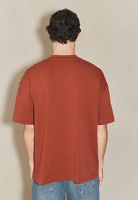 Luźna, rdzawo zabarwiona koszulka z miękkiej bawełny, z krótkimi rękawami, okrągłym dekoltem i prostym dołem.