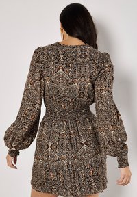Printed dress in dark tones, featuring long puff sleeves, smocked waist, and intricate paisley-like patterns in cream, brown, and navy.