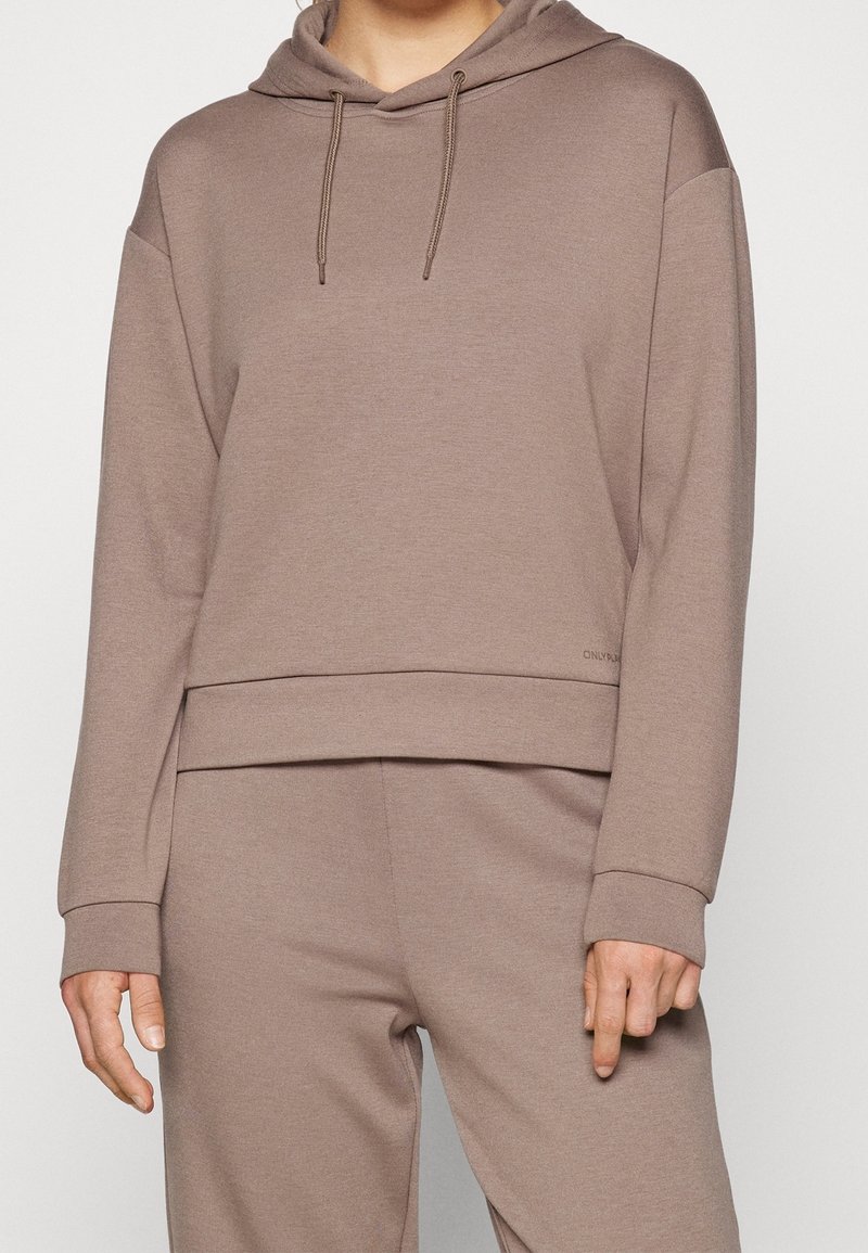 Sudadera con capucha y corte corto en suave tejido beige con puños acanalados y cordón ajustable. Presenta un sutil logo de la marca cerca del dobladillo.