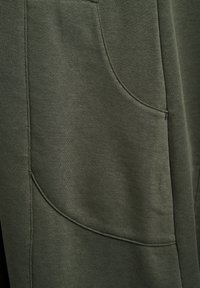 Olive green fabric with a smooth texture and subtle sheen. Features a curved pocket seam and reinforced stitching. Lightweight and stretchy design.