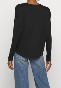 T-shirt noir à manches longues avec un ourlet légèrement arrondi, fabriqué en tissu doux, associé à un jean bleu ample. Les manches sont retroussées au niveau des poignets.