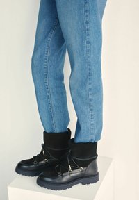 Czarne skórzane i zamszowe botki za kostkę z wiązaniem na sznurowadła, wyściełanym kołnierzem i teksturowaną gumową podeszwą, zestawione z obcisłymi niebieskimi dżinsami.