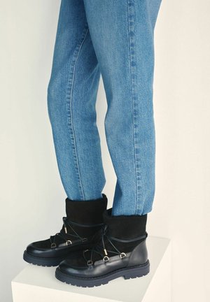 Czarne skórzane i zamszowe botki za kostkę z wiązaniem na sznurowadła, wyściełanym kołnierzem i teksturowaną gumową podeszwą, zestawione z obcisłymi niebieskimi dżinsami.