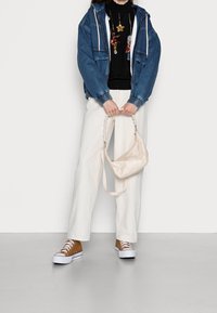 Veste en jean avec poignets élastiques, pull noir avec détails en sequins, pantalon blanc à jambes larges, sac à main beige et baskets marron avec semelles blanches.