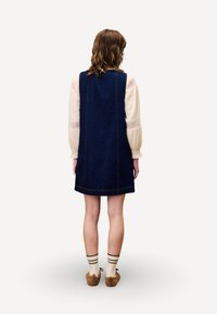 Robe en denim à coupe droite, de couleur bleu foncé, avec des coutures contrastées, associée à une chemise claire et des chaussettes à motif.
