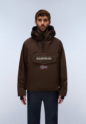 Mand iført en brun hættetrøje Napapijri-jakke med front-lynlåslomme og norsk flaglignende patch, kombineret med mørkeblå jeans.