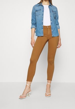 Denim shirt with button-down front, two chest pockets; white fitted t-shirt; tan high-waisted skinny pants; beige strappy heels.