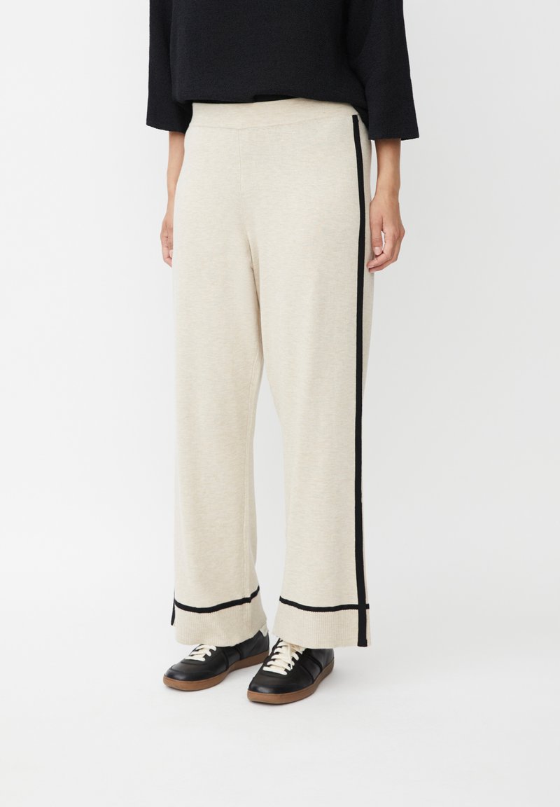 Pantalones de pierna ancha beige con rayas laterales negras, tejido de textura suave y un ajuste relajado, con dobladillo recto y sin herrajes visibles.