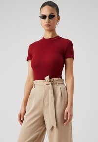 Rode ribbelachtige top met korte mouwen, gecombineerd met beige wijde broek met een riem, voorzien van een gestructureerde stof en een gestrikt detail bij de taille.