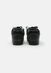 Sorte sneakers med en struktureret suede- og mesh-overdel, polstret krave, flade snørebånd og en tyk gummisål med et logo på hælen.