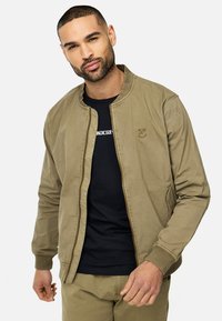 Khaki kurtka bomber z okrągłym kołnierzem, zapięciem na zamek i ściągaczami przy rękawach. Posiada logo na klatce piersiowej oraz gładką fakturę materiału.