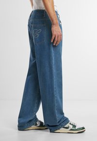 Vaqueros de denim de gran tamaño en azul claro con pierna recta, con costuras en los bolsillos traseros y combinados con zapatillas verdes y blancas.