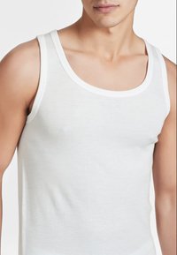 Top bianco senza maniche con scollatura tonda e spalline sottili, realizzato in un tessuto morbido e leggero, caratterizzato da un design aderente.