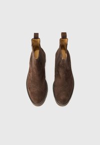 Botas Chelsea de ante marrón con un diseño elegante, puntera redondeada, detalles de brogue decorativos y paneles elásticos en los laterales para facilitar su uso.