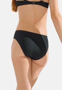 Bas de bikini noir en matériau texturé. Design taille haute avec une couverture modérée et des bords lisses. Les côtés ouverts créent une silhouette élégante.