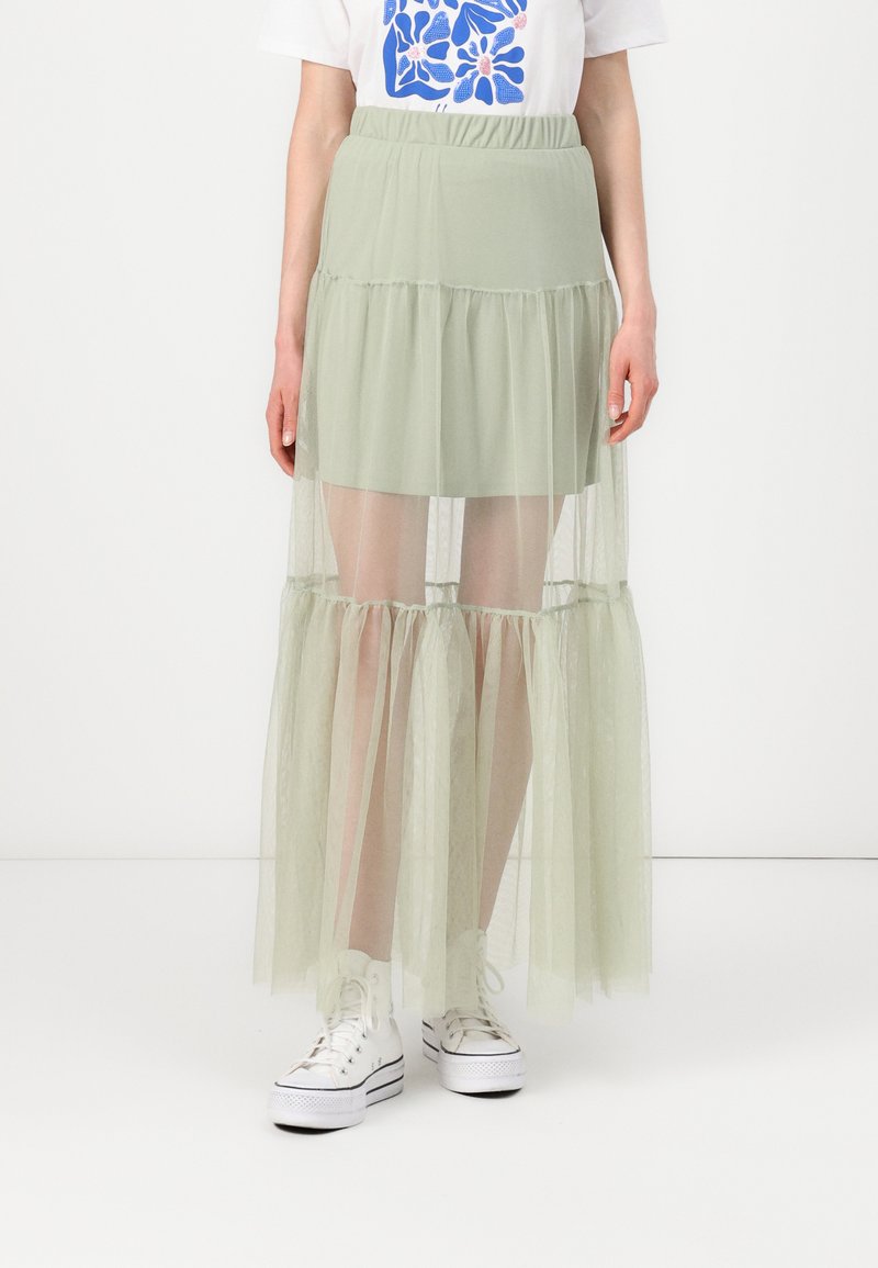 Jupe échelonnée vert clair en tulle transparent, dotée d'une taille élastique et d'une coupe fluide. Associée à des baskets montantes blanches.
