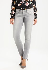 Jean skinny gris avec une texture lisse, taille mi-haute et design à cinq poches, associé à un haut noir à motifs floraux.