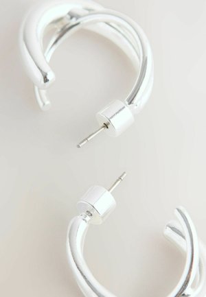 Strieborné kovové náušnice s krúžkovým tvarom a prekrúteným dizajnom, so lesklým povrchom a cylindrickým uzáverom. Hladká textura, moderný tvar.