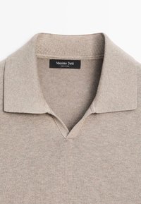 Polo en maille beige avec col côtelé et étiquette noire Massimo Dutti cousue à l’intérieur de l’encolure.
