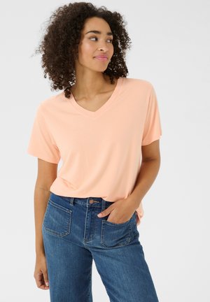 T-shirt pêche à col en V en tissu doux, manches courtes, associé à un jean bleu taille haute avec poches avant et fermeture à bouton.