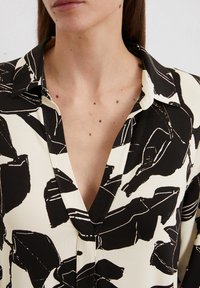 Blusa a righe in bianco e nero con scollo a V profondo, colletto rigido e tessuto morbido decorato con forme e linee astratte.