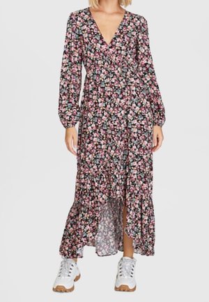 Vrouw die een lange mouw, V-hals jurk met bloemenprint draagt, met een asymmetrische zoom, gecombineerd met witte chunky sneakers.