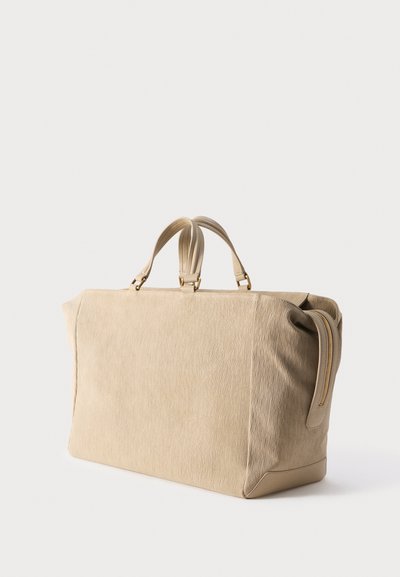 Μεγάλη ορθογώνια υφασμάτινη ταξιδιωτική τσάντα σε μπεζ χρώμα με διπλές χειρολαβές και φερμουάρ σε μία άκρη, εμφανιζόμενη σε απλό ανοιχτό φόντο.