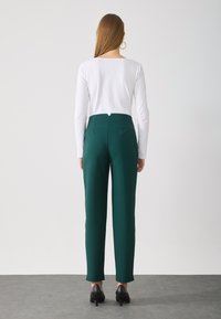 Groene broek met een getailleerde pasvorm, voorzien van een hoge taille en rechte benen, gecombineerd met een witte langslavtop en zwarte hakken.