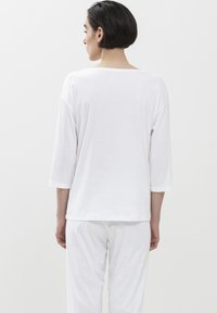 Witte, relaxte 3/4 mouwtop met een wijde halslijn, gemaakt van zachte stof, gezien vanuit de achterkant, gecombineerd met bijpassende witte broek.
