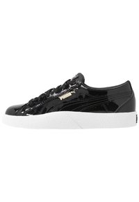 Sneaker in pelle verniciata nera con suola in gomma bianca testurizzata, dotata di lacci neri e logo Puma dorato sul lato. Design a profilo basso.