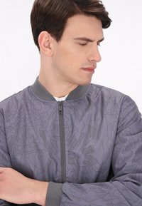 Szara kurtka bomberka z geometrycznym tonalnym wzorem, teksturowanym materiałem, prążkowanym kołnierzem i mankietami oraz zamkiem błyskawicznym z przodu.