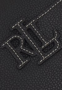 Svart texturerat läder med upphöjda initialer "RL" i en kontrasterande vit sydd kant. Strukturerad design med fina detaljer.