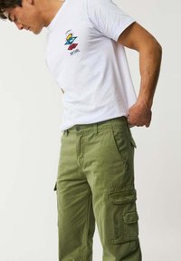 Maglietta bianca in cotone con logo Rip Curl colorato. Pantaloni cargo verde oliva con molteplici tasche e dettagli cuciti.