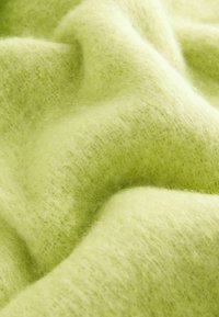 Pehmea kerge rohelise fleece-kangas, millel on karvane tekstuur, õrnad varjundimuutused ja sile, lainetav pind.