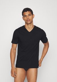 T-shirt noir col en V en tissu doux. Manches courtes, coupe slim, avec un petit logo sur la poitrine. Texture lisse, design minimal.