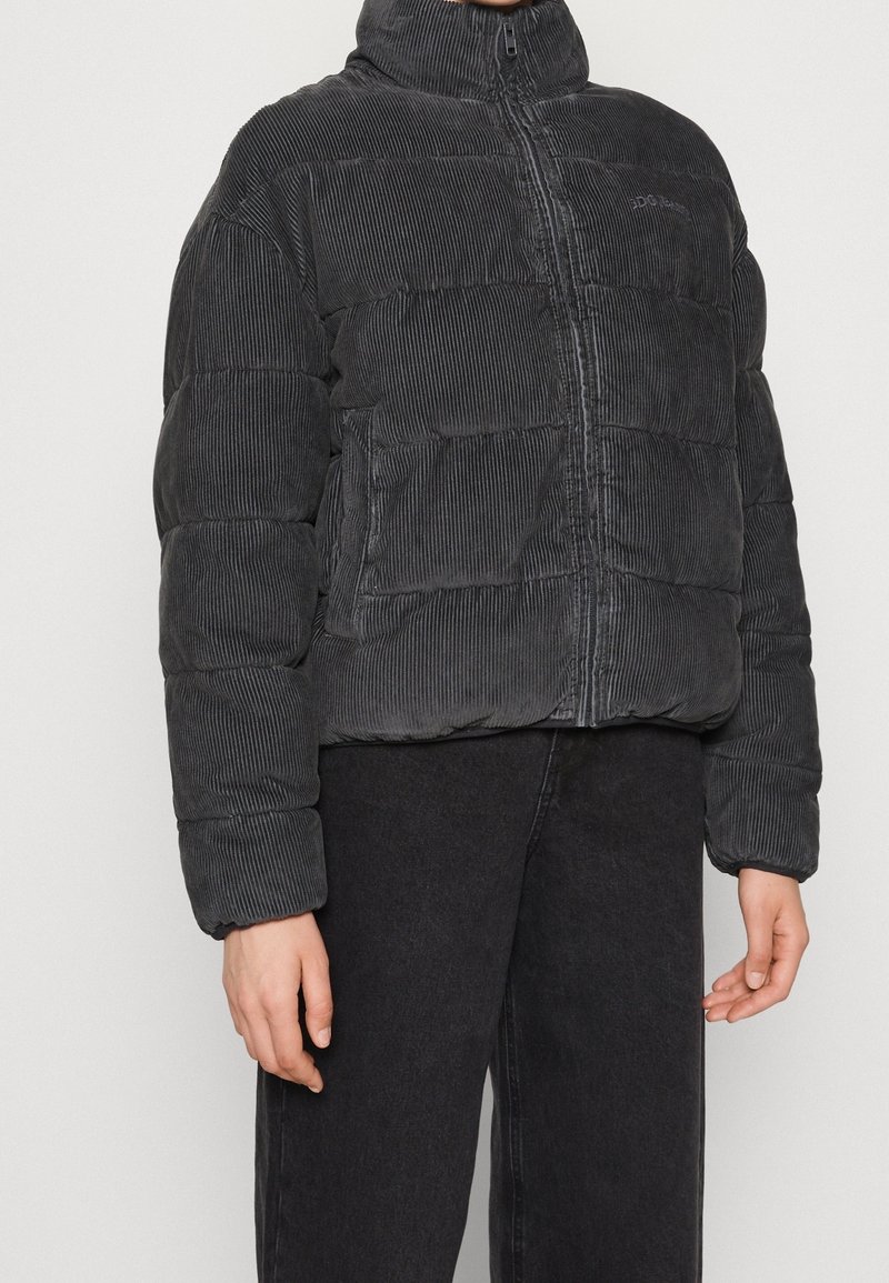 Svart kordfløjl puffjacka med hög krage, framdragkedja och texturerat vertikalt ribbat mönster. Tätt sittande silhuett med sidofickor.