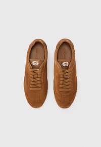 Καφέ σουέτ αθλητικά παπούτσια με στρογγυλεμένη μύτη, υφασμένο πάνω μέρος και κορδόνια στο ίδιο χρώμα. Διαθέτουν λογότυπο στο γλώσσα του παπουτσιού.