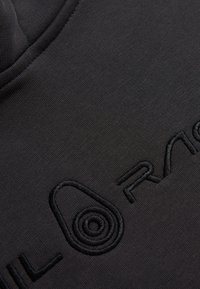 Sudadera negra hecha de una suave mezcla de algodón. Presenta un bordado en relieve negro de un logo en la parte frontal, con un detalle de diseño redondo.