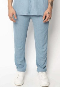 Pantalons en coton bleu clair avec une finition texturée, offrant une coupe décontractée et une taille élastique, associés à des baskets blanches.