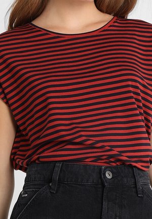 Frau trägt ein rot-schwarz horizontal gestreiftes Kurzarmshirt, das in eine hoch taillierte schwarze Jeans aus Denim gesteckt ist.