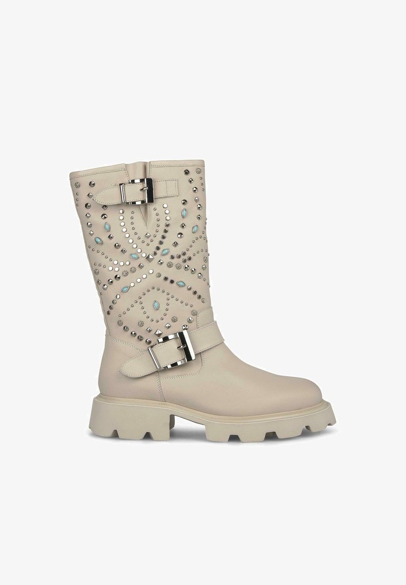 Beżowe, skórzane kozaki do kolan z elementami dekoracyjnymi w postaci ćwieków i bocznym zapięciem na klamrę. Gruba podeszwa z teksturowanym bieżnikiem.