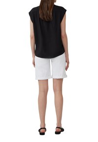 Haut noir à manches courtes avec une finition texturée, associé à des shorts blancs à ourlet roulé. Le modèle porte des sandales noires, vu de dos.