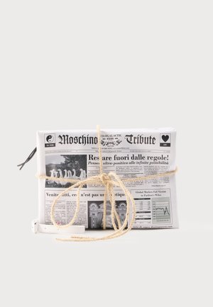 Witte clutch tas ontworpen als een gevouwen krant met zwarte tekst en afbeeldingen, vastgebonden met een beige koordstrik en een witte polsband.